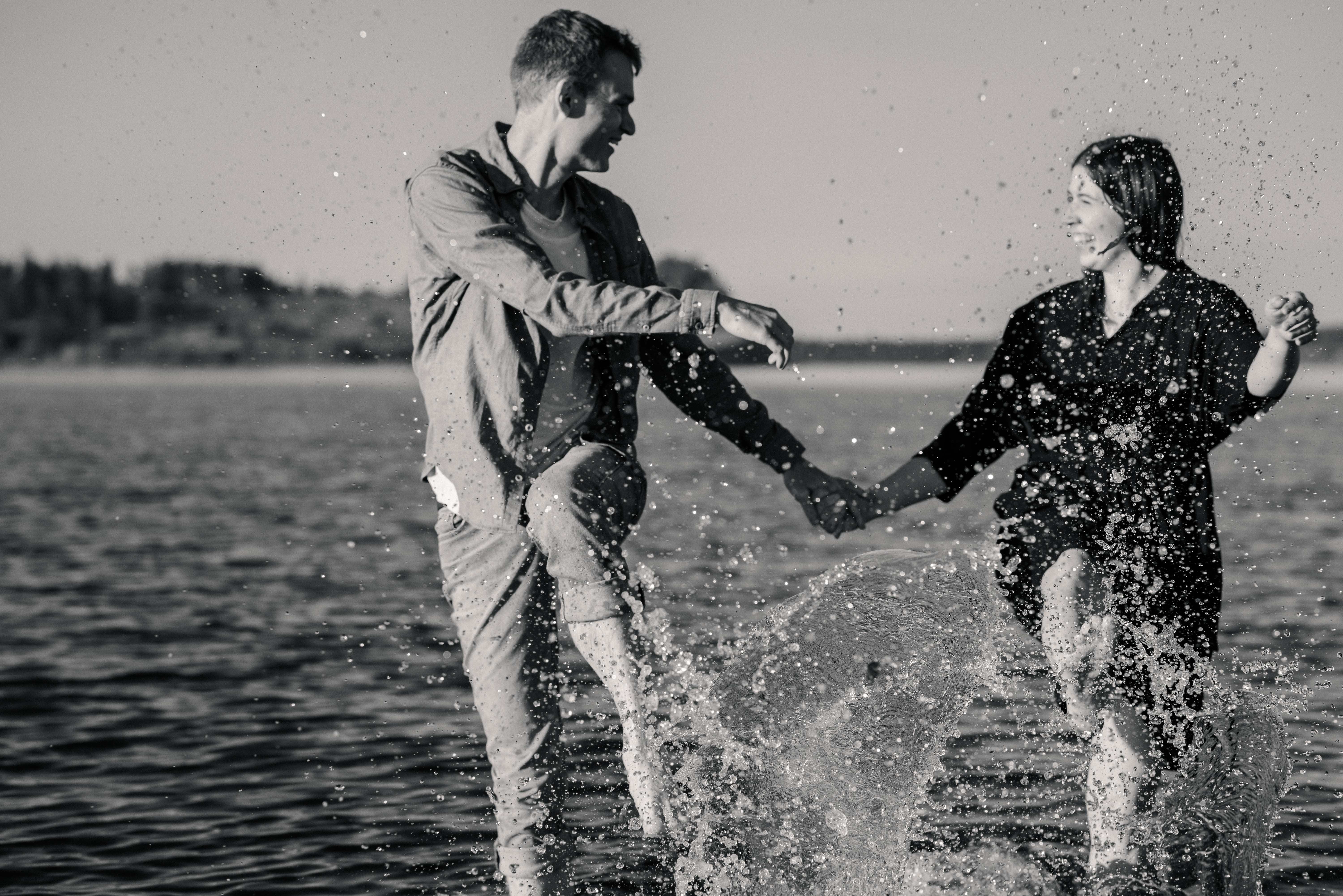 A candid moment of a couple laughing as they splash water at Island View Beach on Vancouver Island