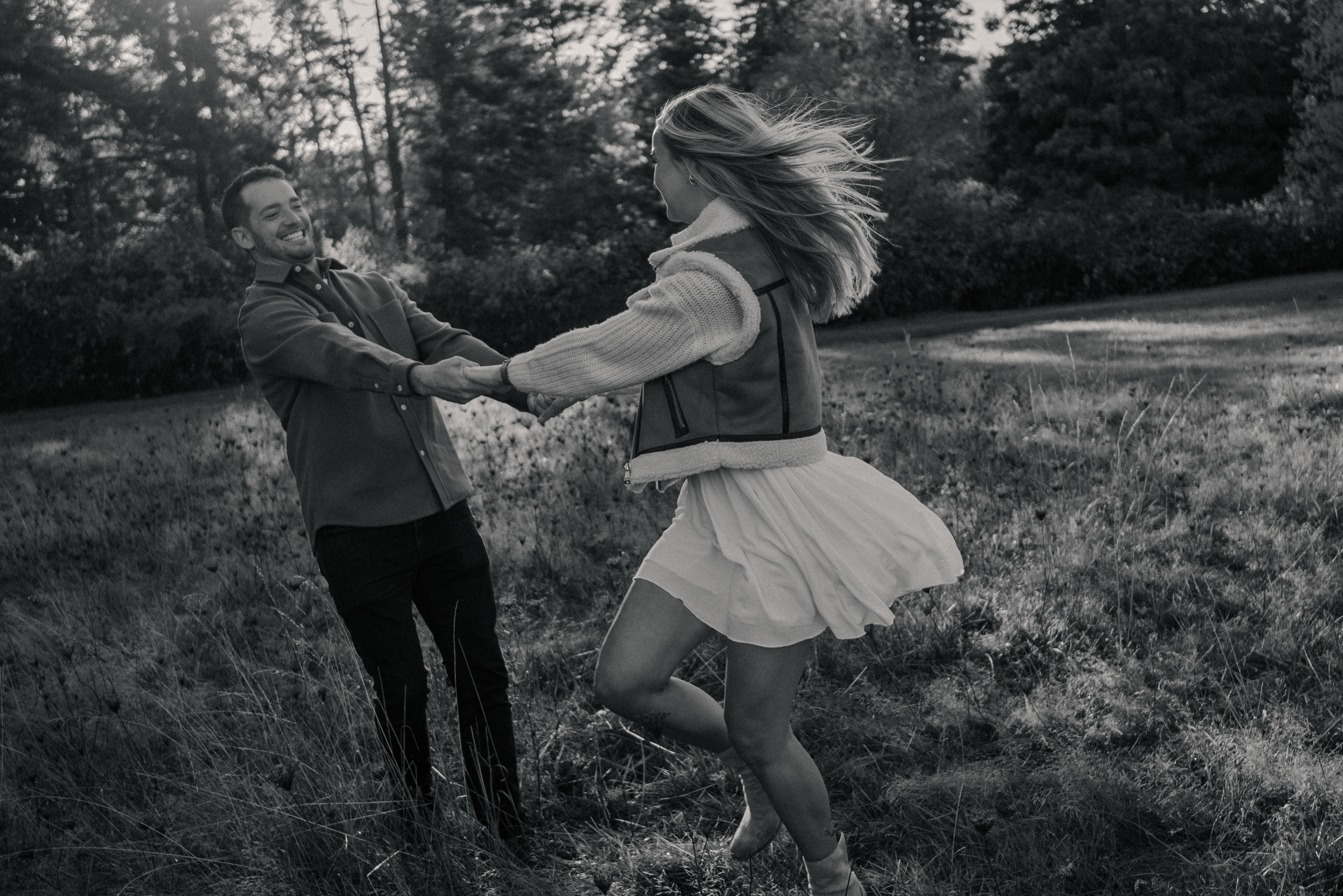 Candid photo of a couple holding hands and spinning around together in a grassy field at Devonian Regional Park, both smiling widely and laughing.