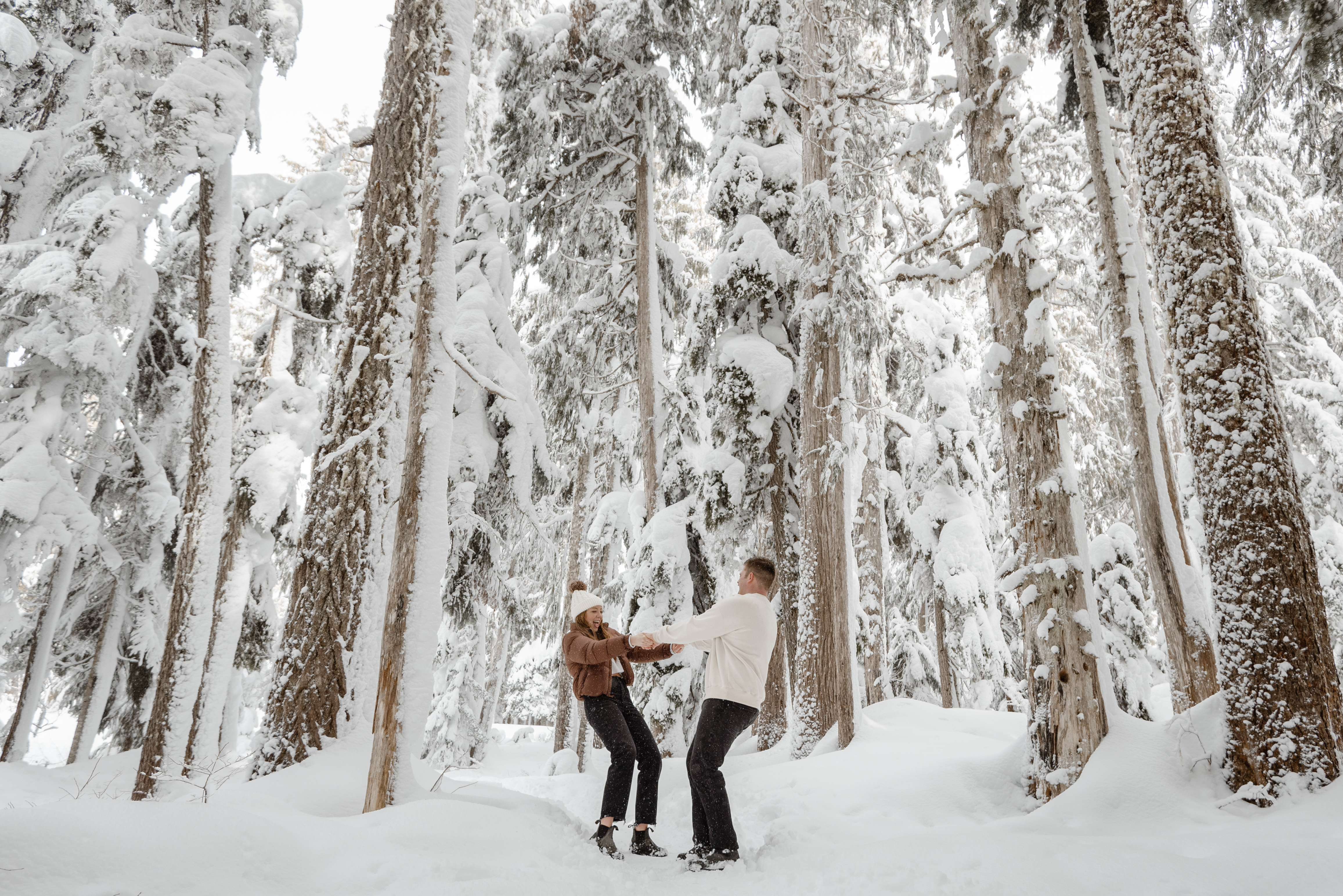 Couple spins around holding hands under snow covered trees at Mount Washington Resort, Vancouver Island