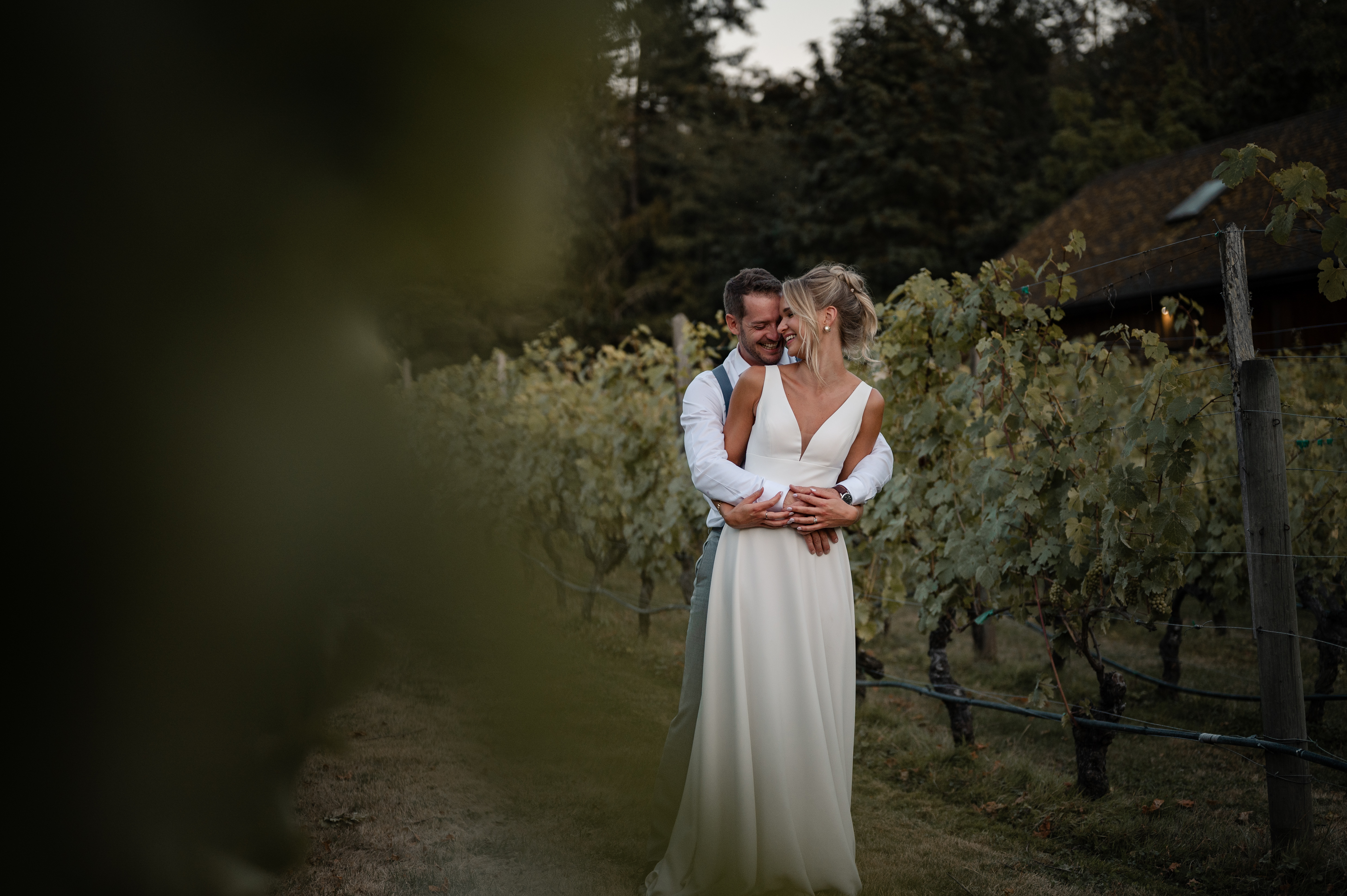 Couple stands in the vineyard embracing in laughter at Deep Cove Winery