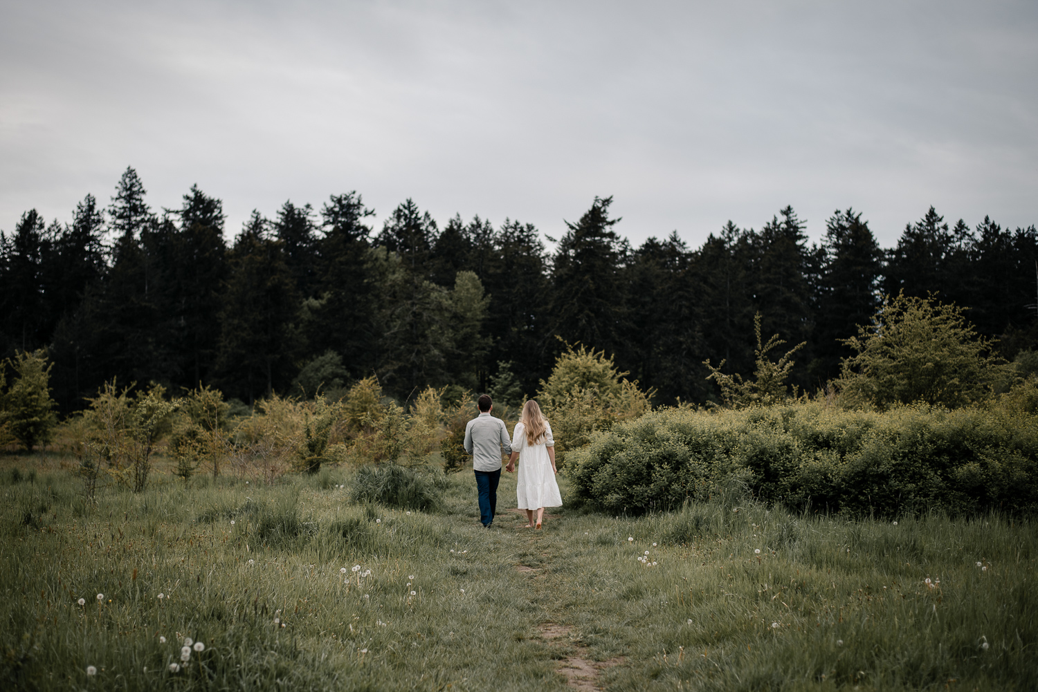 A couple walks in a lush green feild at Elk & Beaver Lake on Vancouver Island