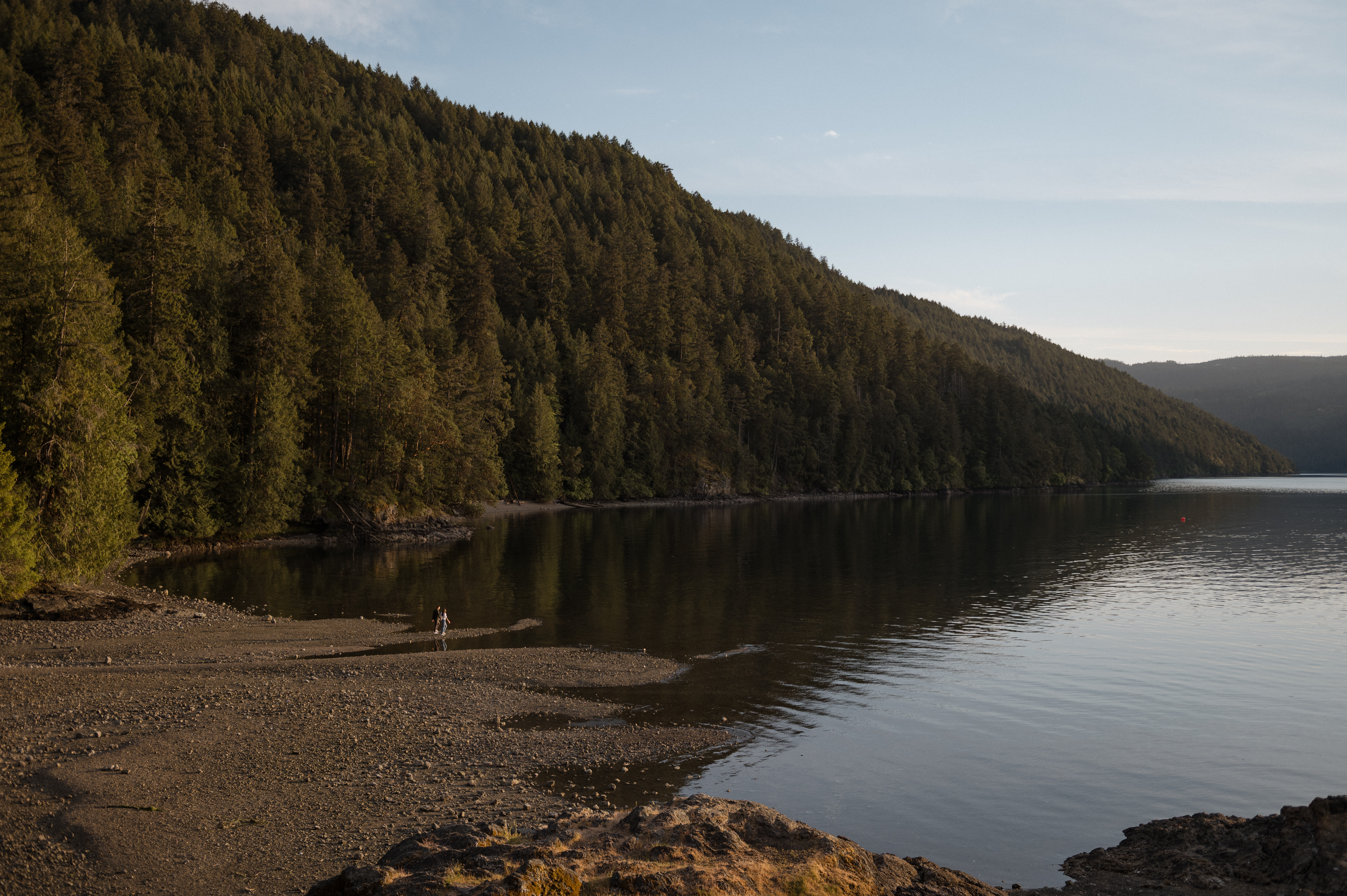 Couple walking toward the shoreline at McKenzie Bight on Vancouver Island, appearing small within a wide coastal landscape.